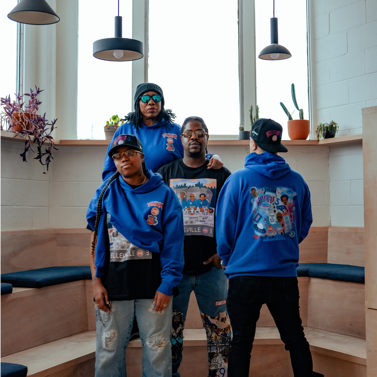 Four people wearing blue hoodies with a graphic design in a modern indoor setting.
