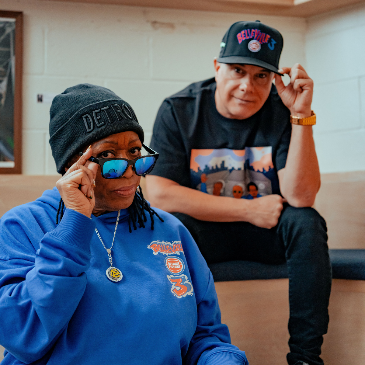 Two people wearing Detroit-themed clothing and hats in a casual setting.